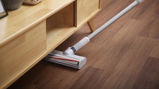 Vacuum cleaning wooden floors under sideboard to show how often you should vacuum floors