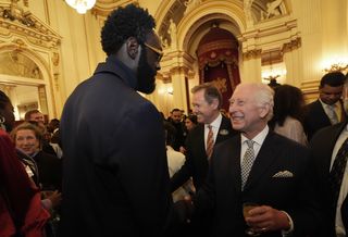 King Charles shaking the hand of a tall male guest wearing sunglasses and a dark suit at a Buckingham Palace reception for TV and film stars