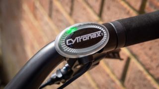 The clear plastic control button from the Cytronex e-bike conversion kit, with a white Cytronex logo in the centre of a black circle mounted to the handlebar of a bike