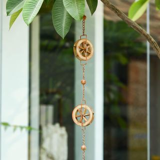 A decorative rain chain featuring a wheel design hung in a garden