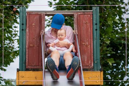 Parent going down slide with baby on knee