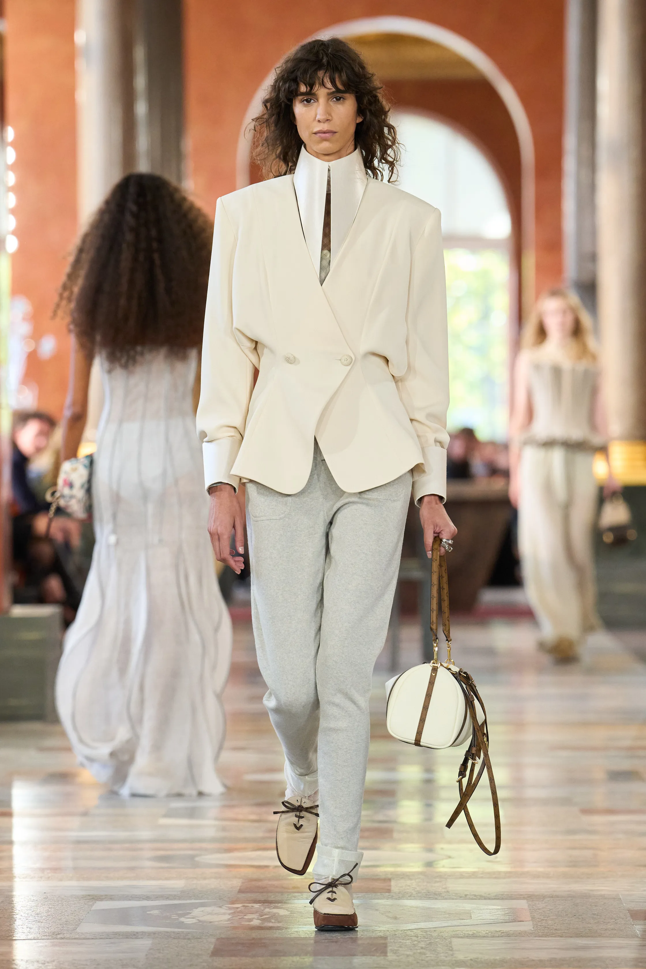 a model on Louis Vuitton&#039;s Spring 2026 runway wearing gray best sweatpants, a white stiff shirt, white blazer, white leather bag, and lace-up white shoes
