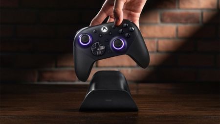 An 8BitDo Ultimate 3E controller being picked up from its charging stand