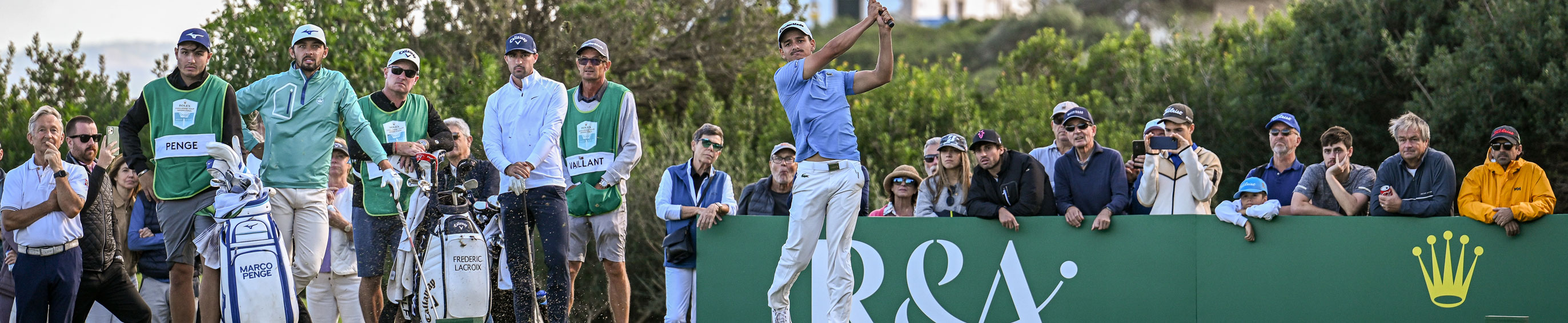 A golfer hits a tee shot whilst surrounded by players and fans