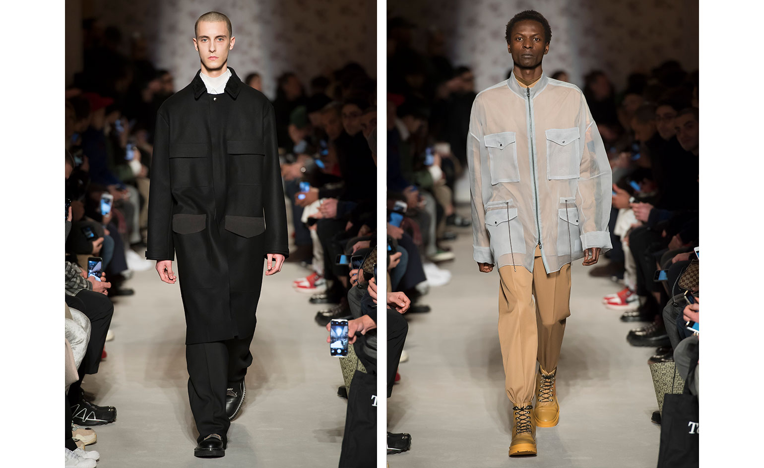 Catwalk view of two models wearing looks from OAMC's collection. One model is wearing a white top, black coat, black trousers and black boots. And the second model is wearing a light brown top, a light blue semi-transparent piece with pockets over the top, light brown trousers and dark yellow boots. There are people seated on both sides of the catwalk