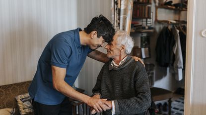 A young man touches foreheads with an older man in a caregiving situation.