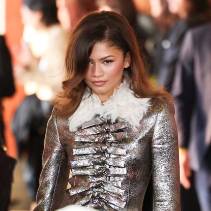 a woman with brown hair posing for a camera while wearing a metallic jacket with feather trim