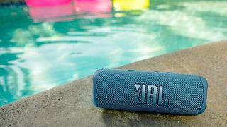 The JBL Flip 6 portable speaker in pale blue pictured next to a swimming pool.