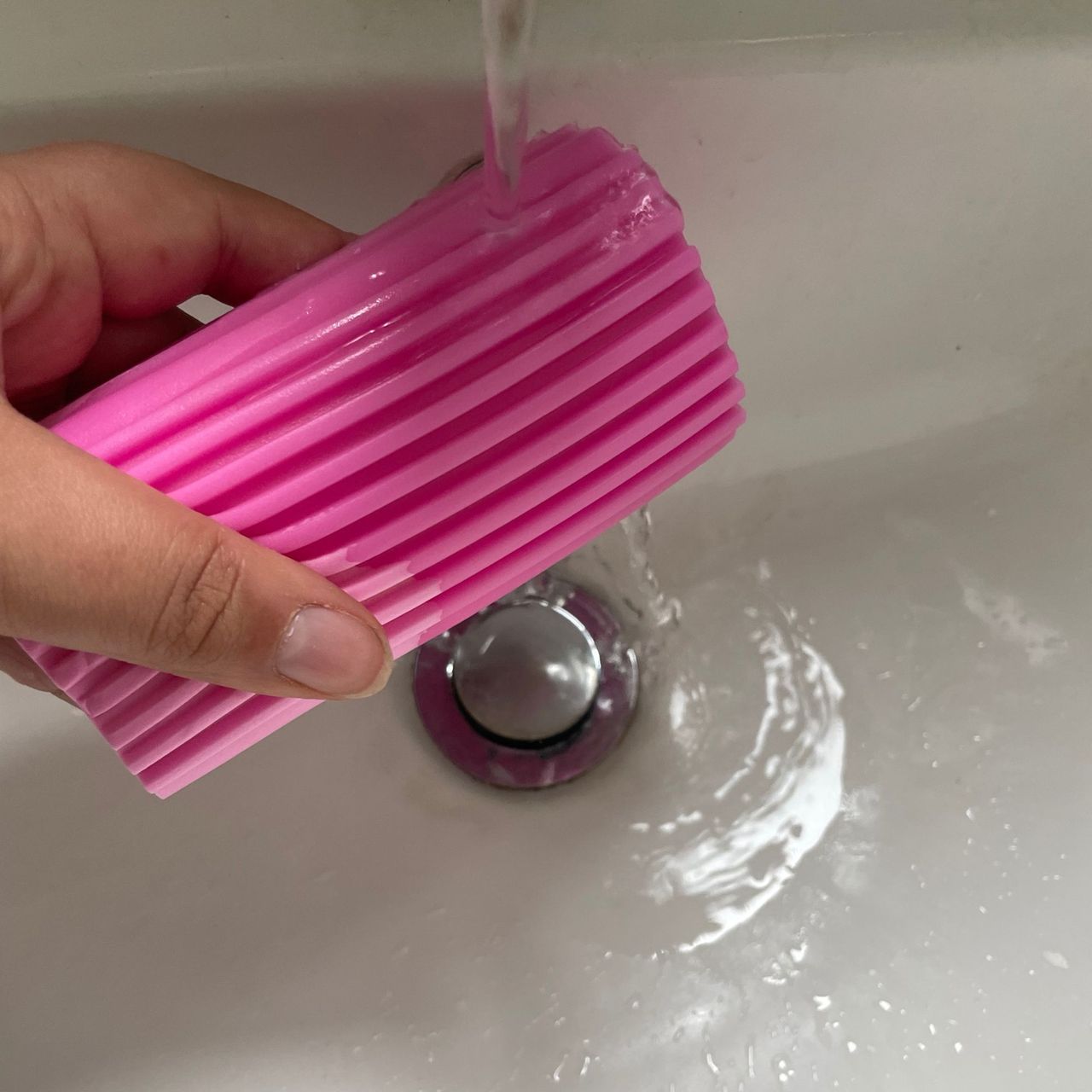Holding pink Damp Duster under running water in a white sink with silver plug hole