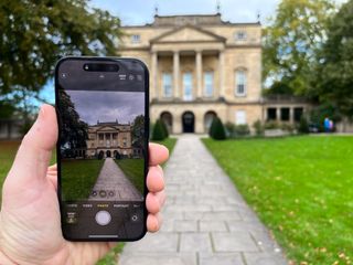 iPhone 15 held in a hand in front of a building