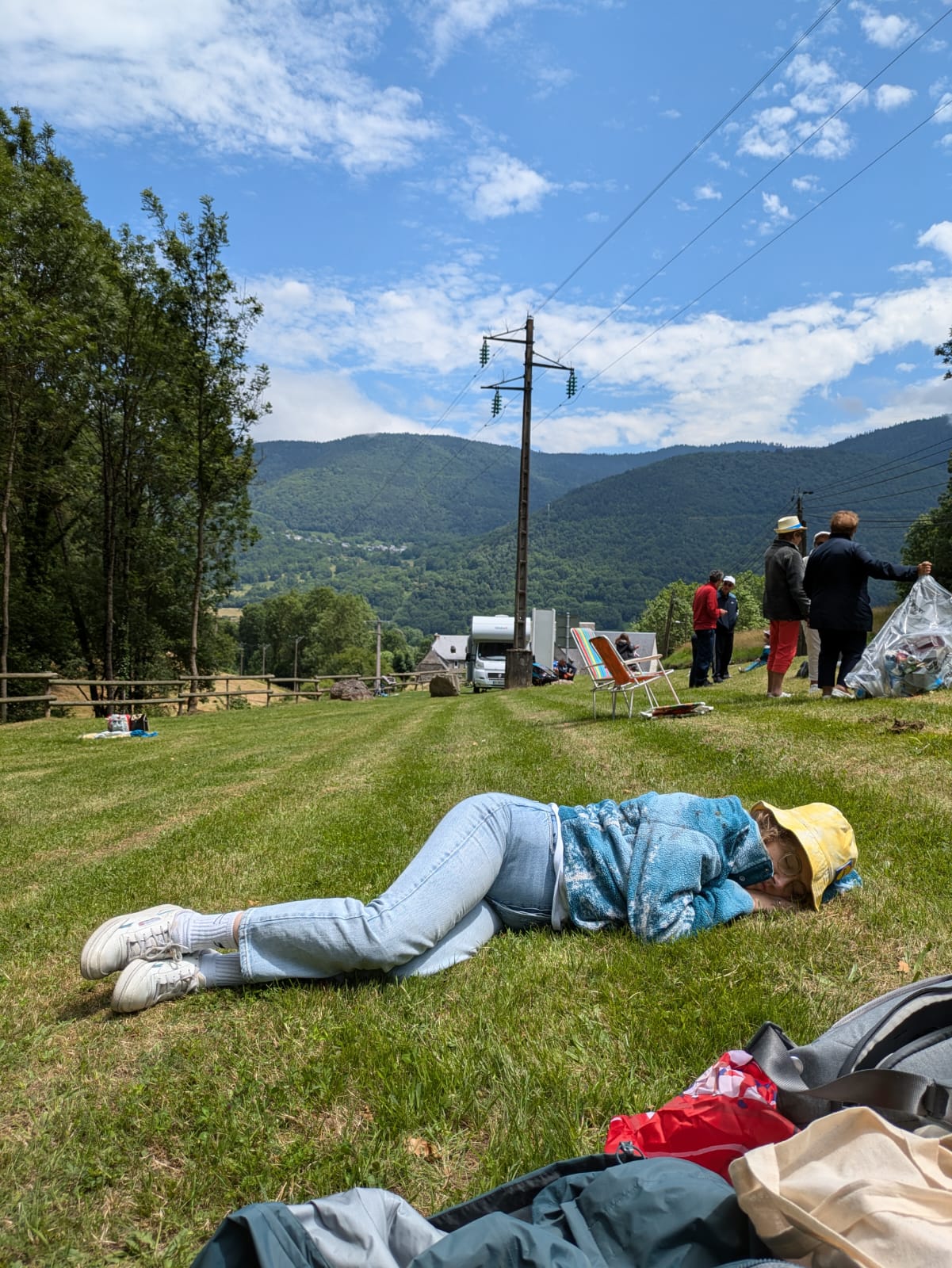 A person lying on the grass asleep, with mountains of the Tour de France in the background