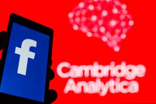 The Facebook logo on a phone in front of a large background with Cambridge Analytica