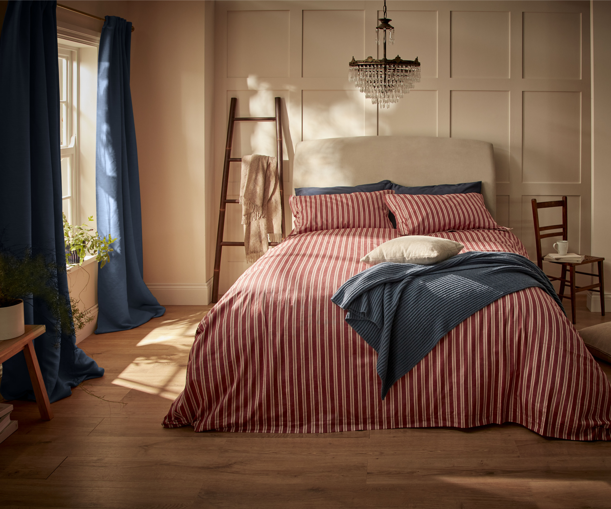 red and white striped bed linen on bed with cream headboard and blue throw