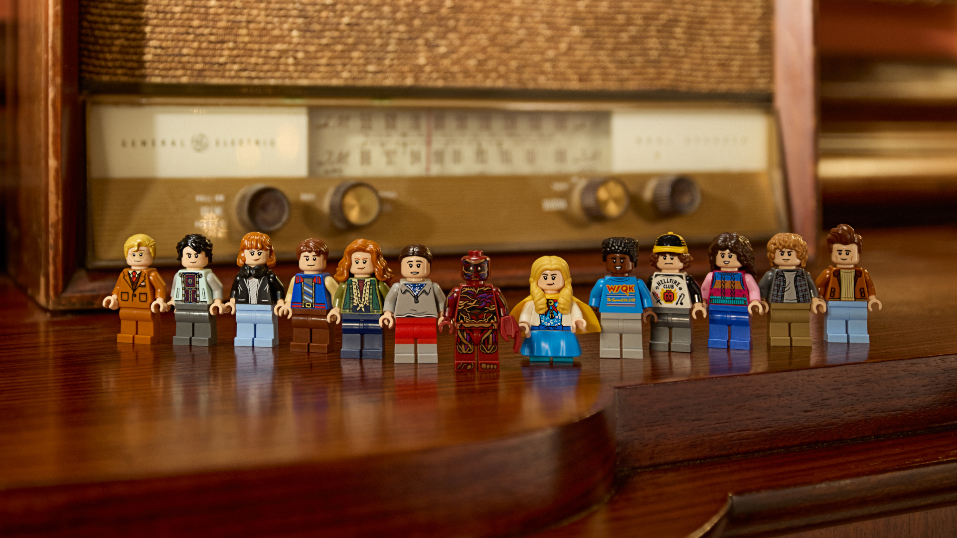 The Lego Creel House minifigures, laid out on a wooden surface in front of a 1950s radio