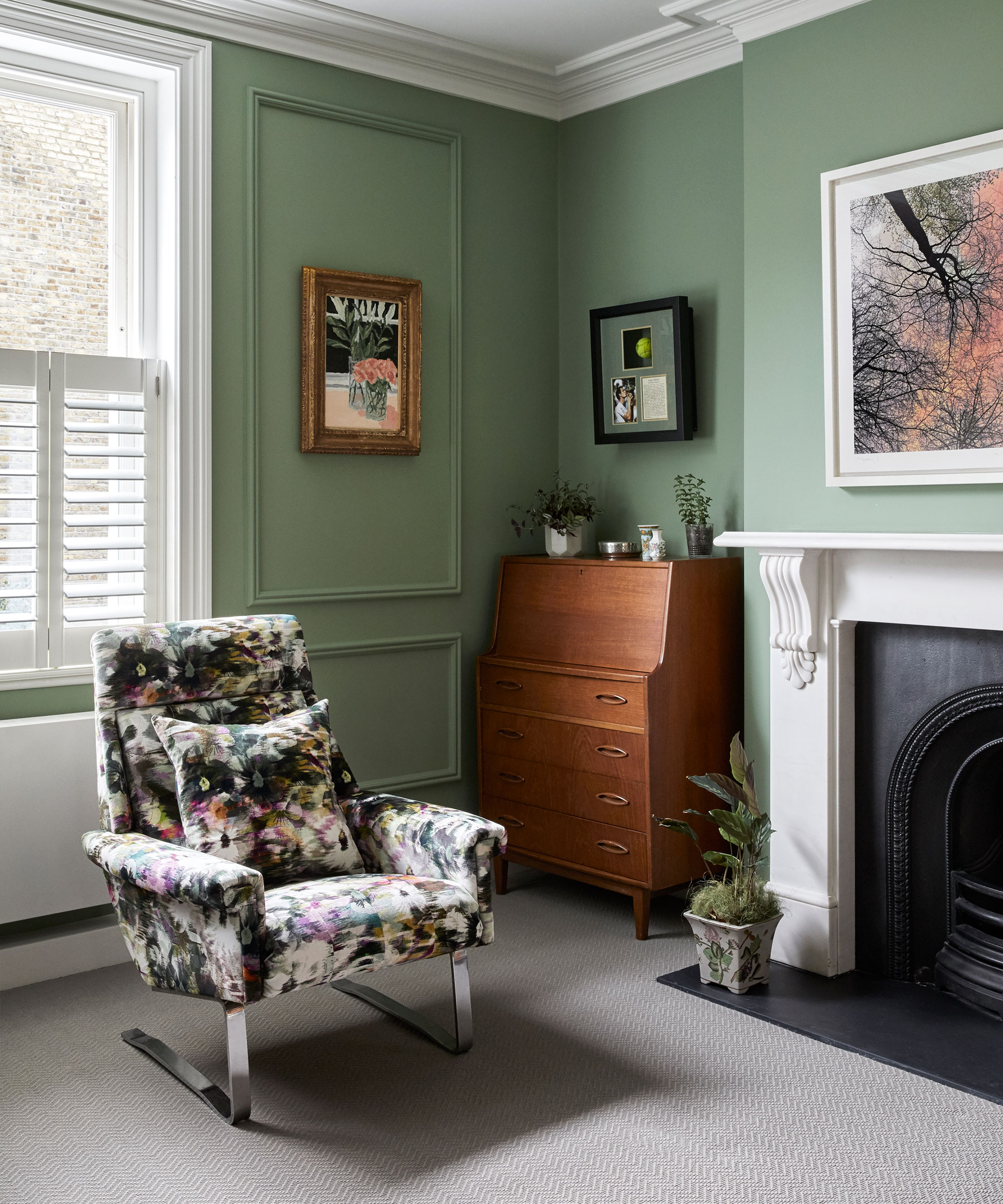 Small green living room decor ideas with green panelled walls, white window frames and fireplace, floral rocking chair and wooden bureau desk