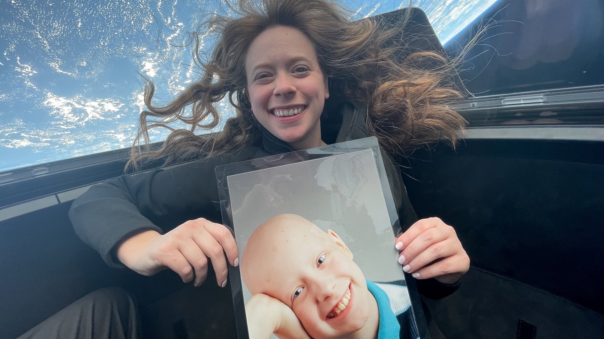 woman floating in orbit with earth behind, holding a childhood picture