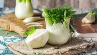 Fennel bulb sitting on table on hessian sack with half cut fennel placed beside