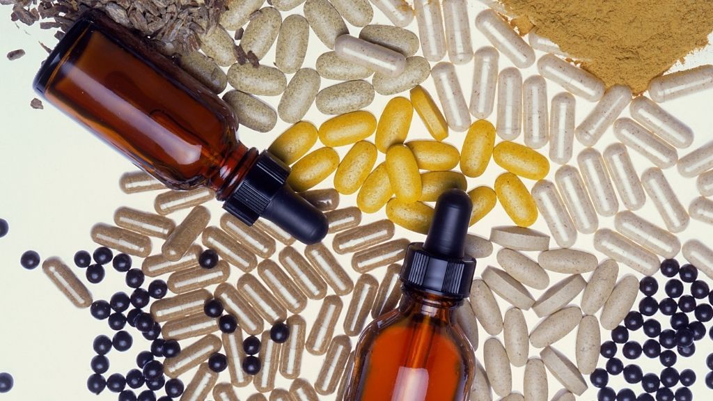 loose supplement capsules, pills and small oil-filled bottles strewn on a white table