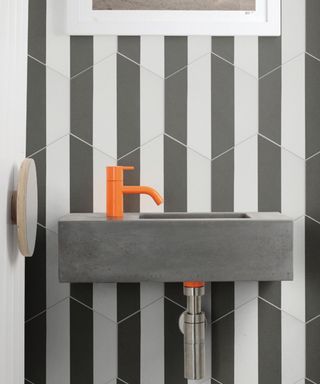 Striking and graphic bathroom with mono stripe effect wall tiles, concrete sink, and orange pop tap