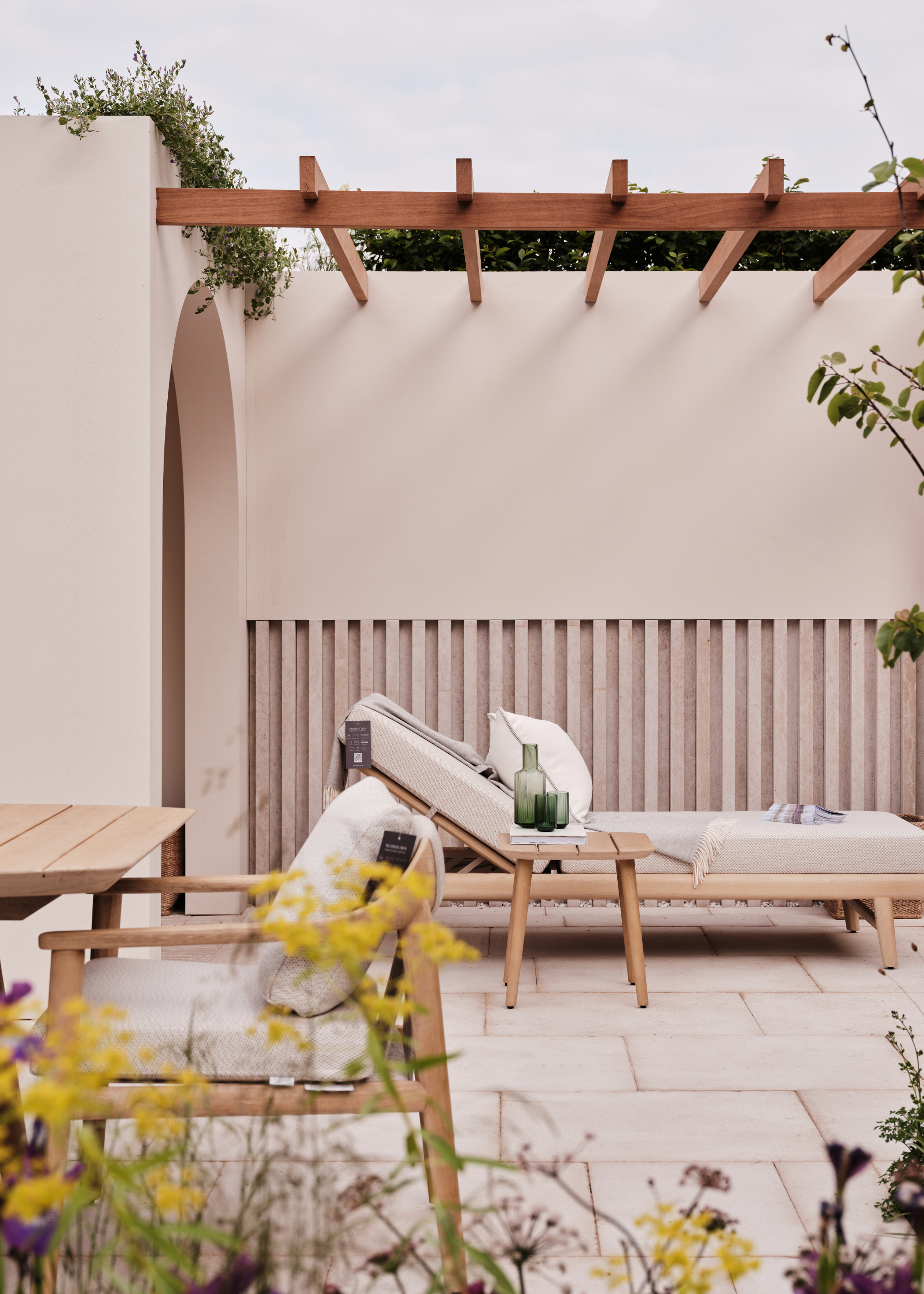 A still from Nth Degree's exhibit at the 2025 Chelsea Flower Show featuring an outdoor lounging daybed and a side table with a glass carafe and a set of matching green glasses