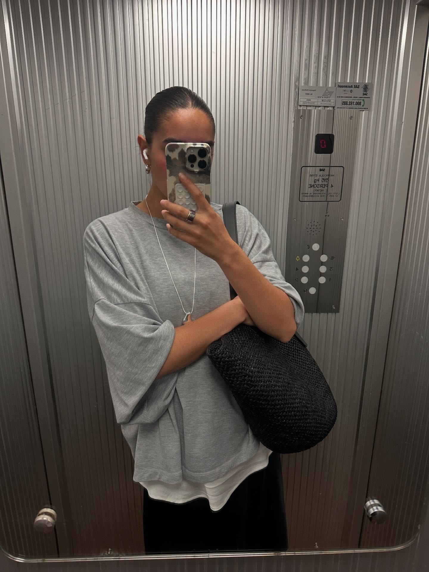 A woman wearing a gray oversized tee, black skirt, and a large black woven tote.