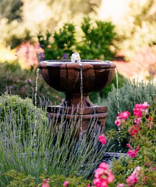 Rustic Italian-style cast concrete garden fountain with pink roses in foreground