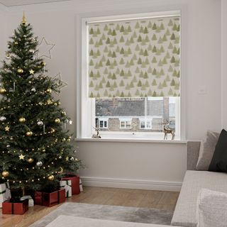 A Christmas tree stands in front of a Christmas themed blind