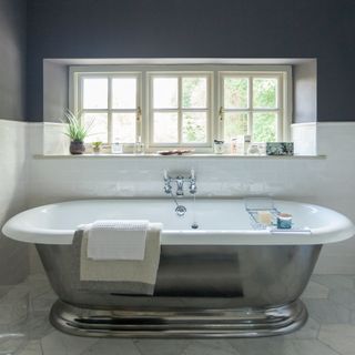 Silver roll top bath tub in bathroom with hexagonal tiled flooring and metro tiled wall