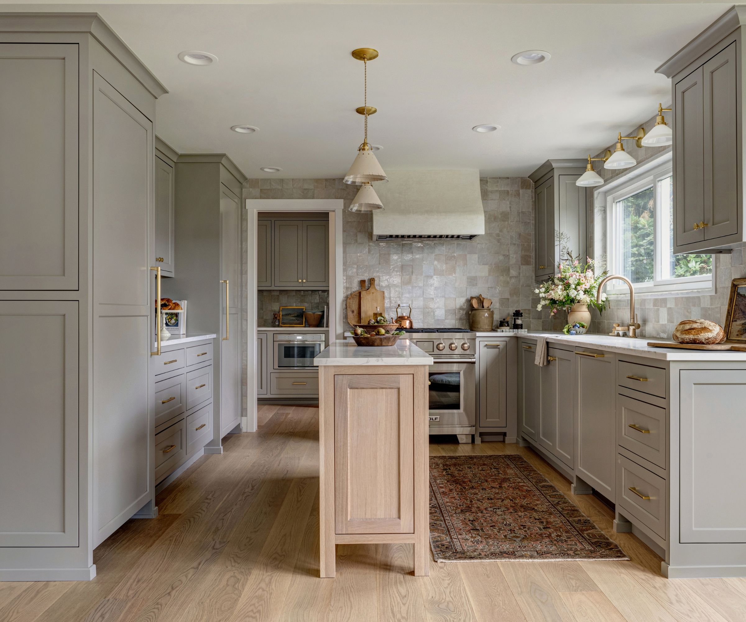 A kitchen with gray cabinets, a wooden island, zellige wall tiles, and brass hardware