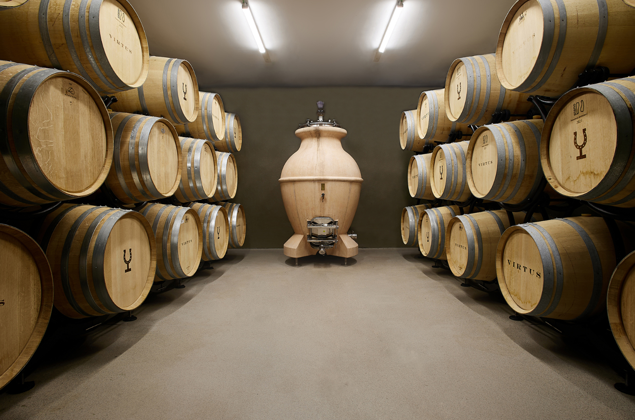 A room with oak barrels on the left and right side, and a large round ceramic amphora