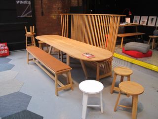 Three round wooden stools, displayed next to a long table with matching bench