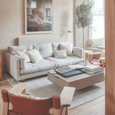 A bright living room with a low cream sofa and two wooden chairs
