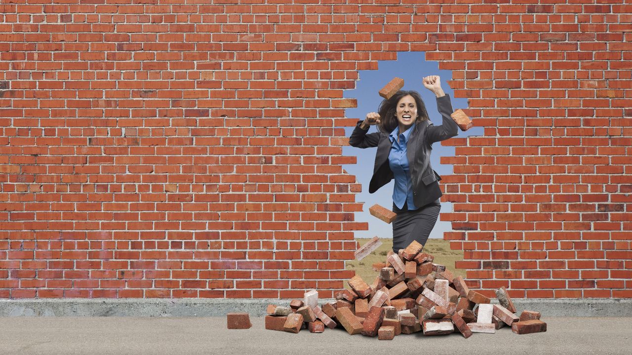 A determined-looking woman breaks through a brick wall.