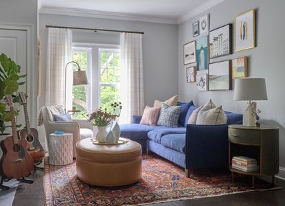 pale gray living room with blue sectional, leather footstool, vintage rug, gallery wall