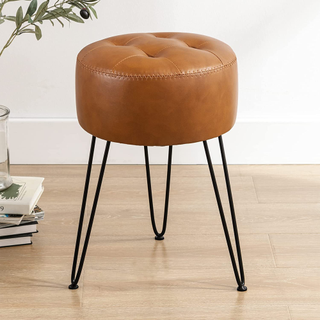 A brown faux leather round vanity stool with black legs