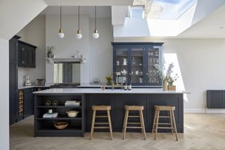 A dark blue kitchen with display cabinets and pendant lighting overhead