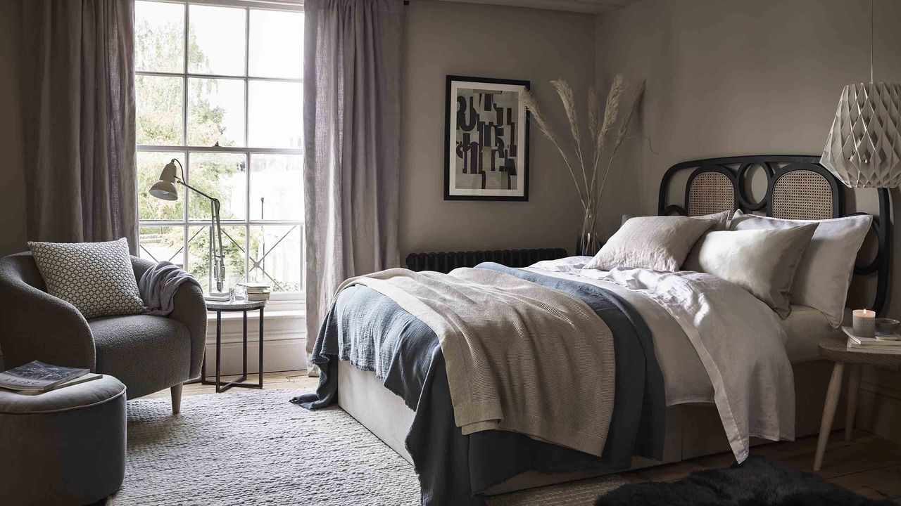 A large bedroom with desk lamp, jute rug, Terrazzo side table, grey velvet, rattan headboard, sheepskin Rug, silk pillowcases on bed and pendant ceiling light.