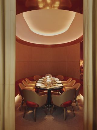 A 1970s-inspired private dining room in a restaurant features leather chairs and a central wooden table covered in golden serveware, a textural ceiling, and wooden walls.