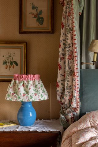 trad bedroom with floral bedding, curtain and blue base light with floral fabric lampshade