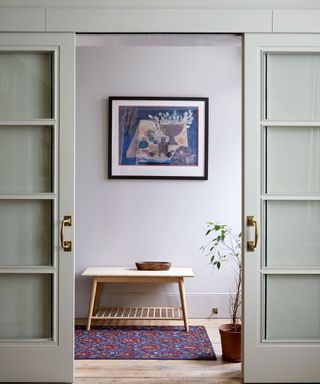 Looking through two gray sliding doors into hallway with wooden floor, wooden bench, rug, framed artwork