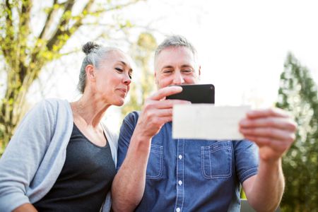 An older couple smiles at a check as they scan it with a cellphone for a direct deposit. The photo may symbolize guaranteed income in retirement.