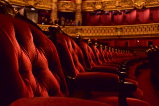 A close up of theatre seats in a grand, red and gold theatre.