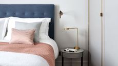 bedroom with navy blue headboard, white and pink bedding and bedside table