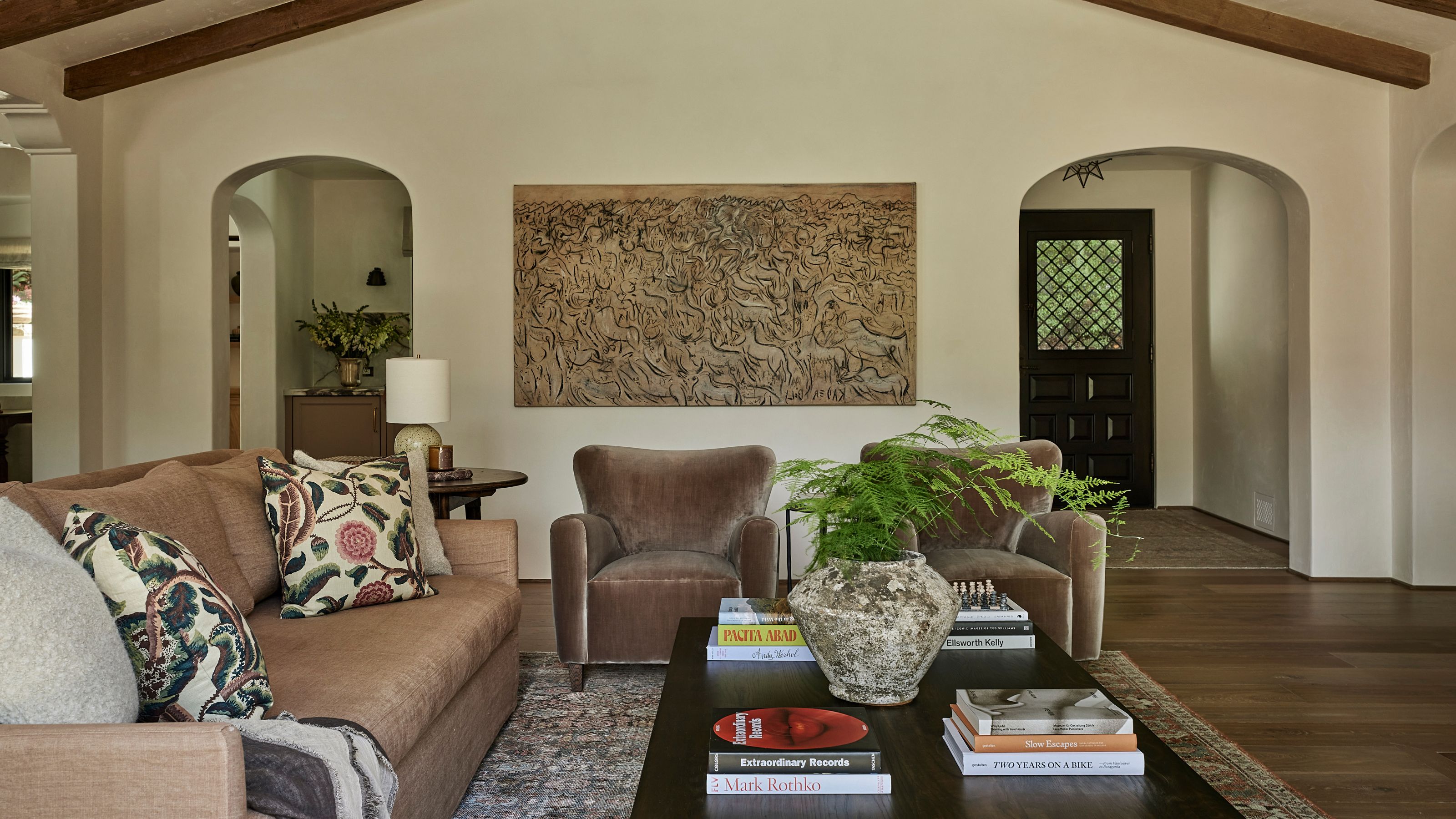 a large neutral open plan living area with vaulted beamed ceiling, a dusty pink linen couch, two velvet armchairs and a black wooden coffee table