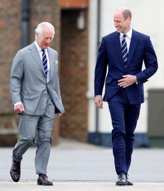 King Charles and Prince William laugh while walking together wearing suits and matching ties