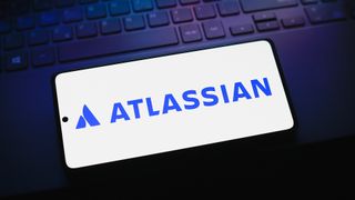 Atlassian logo and branding in blue lettering pictured on a smartphone screen placed on top of a keyboard.