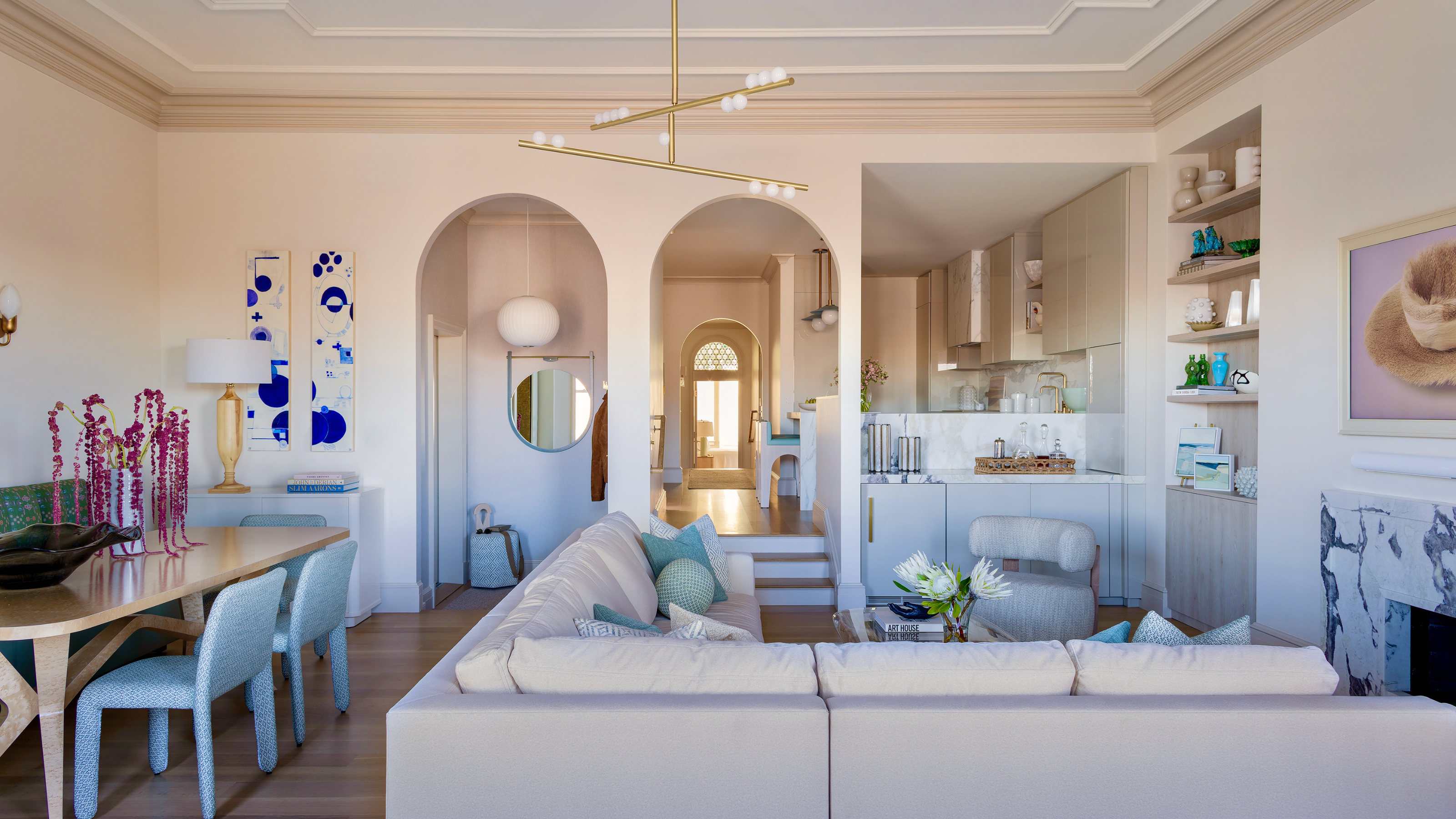 A peach-toned modern living room with two arched doorways in the center of an open living area with an l-shaped sofa, a banquette seating area and a compact kitchen