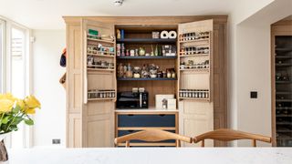 White contemporary kitchen with wooden pantry units with doors open , showing cupboard ingredients