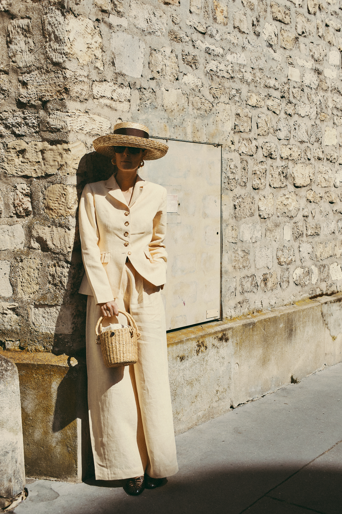 Maria de la Orden wears a matching beige suit and leans against a brick wall in the sunshine.