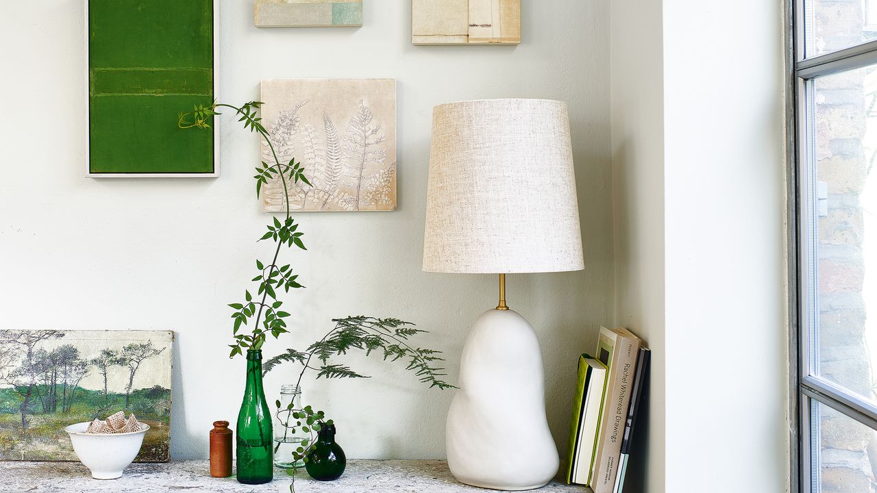 Wooden sideboard with white lamp, glass vases and art on wall